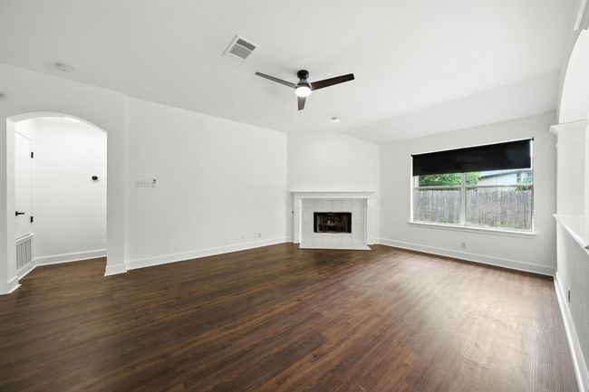 Living room with lofted ceiling, a ceiling fan, a tile fireplace, wood finished floors, and arched walkways | Image 9