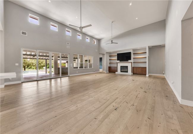 Unfurnished living room with a high ceiling, ceiling fan, plenty of natural light, light wood finished floors, and built in shelves | Image 6