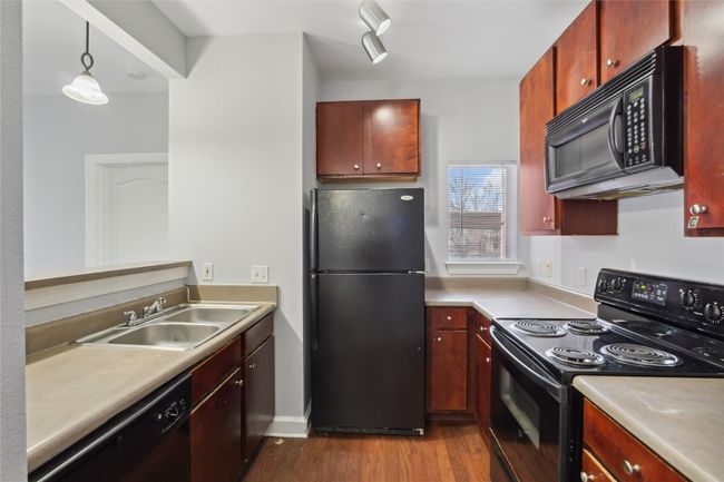 Kitchen with dark wood-style floors, a sink, black appliances, light countertops, and decorative light fixtures | Image 8