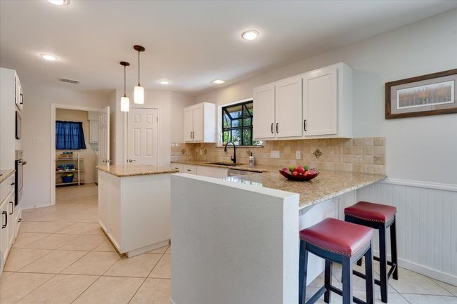 Kitchen featuring a sink, an island, peninsula, backsplash, white cabinetry, and appliances with stainless steel finishes | Image 12