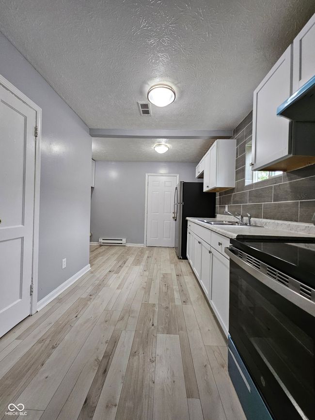 kitchen with black / electric stove, white cabinets, a baseboard heating unit, backsplash, and baseboards | Image 11