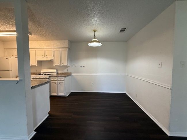 Kitchen featuring white appliances, dark wood-style floors, white cabinetry, a textured ceiling, and decorative light fixtures | Image 4
