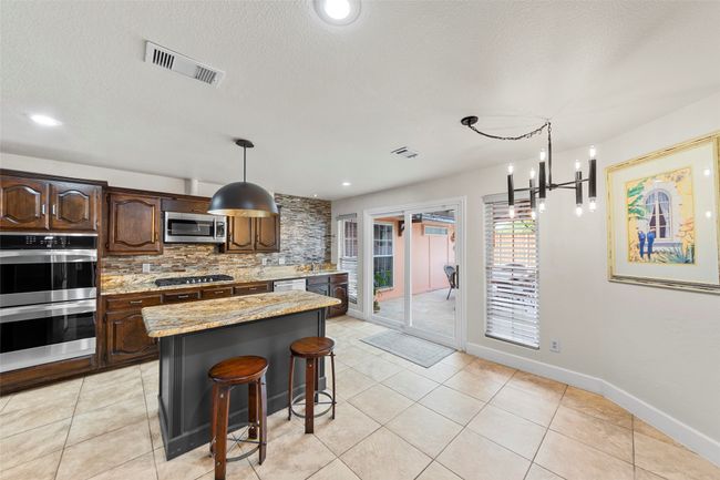 Kitchen with light stone counters, a breakfast bar area, appliances with stainless steel finishes, visible vents, and backsplash | Image 4