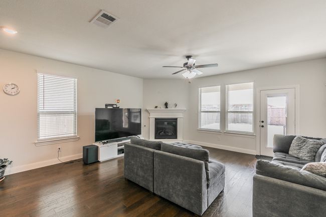 Living room with a ceiling fan, visible vents, baseboards, dark wood-style flooring, and a glass covered fireplace | Image 21