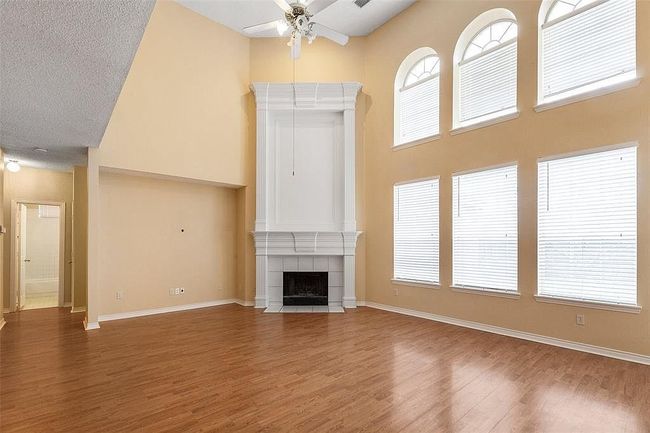 Unfurnished living room featuring wood finished floors, ceiling fan, a towering ceiling, a tiled fireplace, and baseboards | Image 5