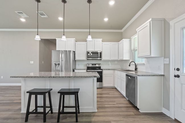 Kitchen featuring stainless steel appliances, a kitchen island, tasteful backsplash, light stone counters, and ornamental molding | Image 11