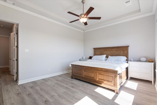 Bedroom featuring light wood-style floors, crown molding, a raised ceiling, a ceiling fan, and baseboards | Image 20