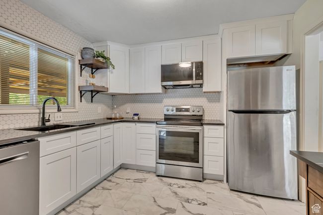 Kitchen featuring appliances with stainless steel finishes, light marble finish floors, white cabinetry, open shelves, and backsplash | Image 5