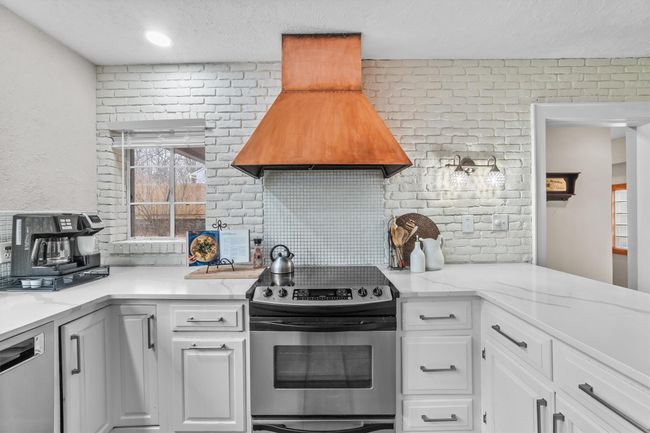 Kitchen with custom range hood, tasteful backsplash, stainless steel appliances, white cabinets, and quartz countertops | Image 13
