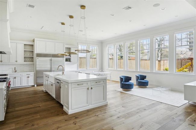 A culinary masterpiece, this gourmet kitchen features a striking Opal White Marble island that flows effortlessly into the breakfast nook. Designed with both style and function in mind, it boasts top-of-the-line appliances, including a state-of-the-art Wolf oven. The eye-catching Bianco Dolomite marble backsplash and custom vent hood seamlessly complement the elegant neutral-tone cabinetry, creating a space that is as sophisticated as it is functional. | Image 11