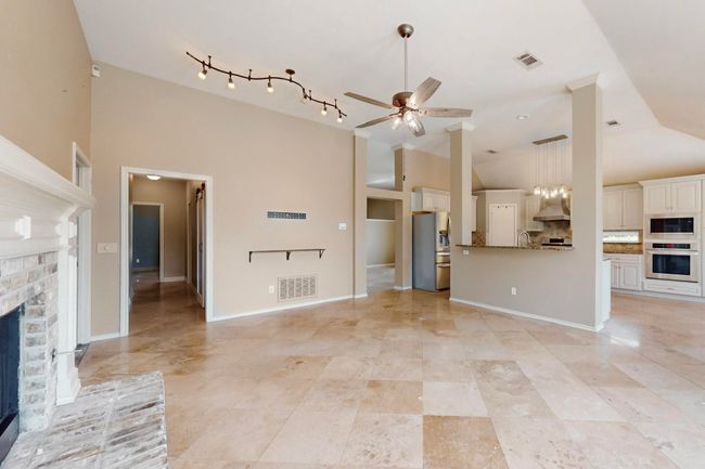Unfurnished living room with high vaulted ceiling, ceiling fan, a brick fireplace, and visible vents | Image 10