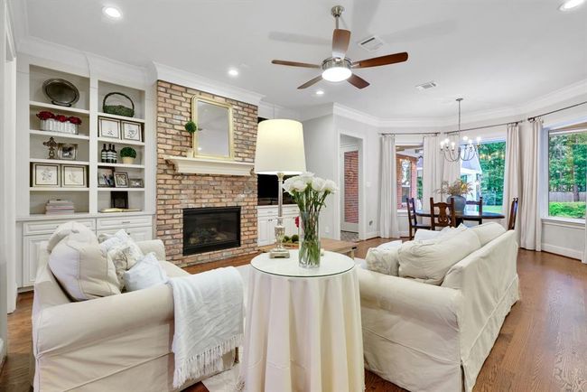 The room is finished with double crown moulding, a modern ceiling fan, and recessed lighting, all set against warm hardwood flooring. Bay windows allow for an abundance of natural light and offer picturesque views of the lush outdoor oasis, adding to the room’s light and airy ambiance. | Image 11
