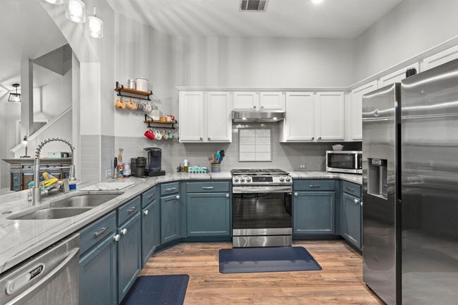 Kitchen featuring light wood finished floors, stainless steel appliances, under cabinet range hood, white cabinetry, and a sink | Image 8