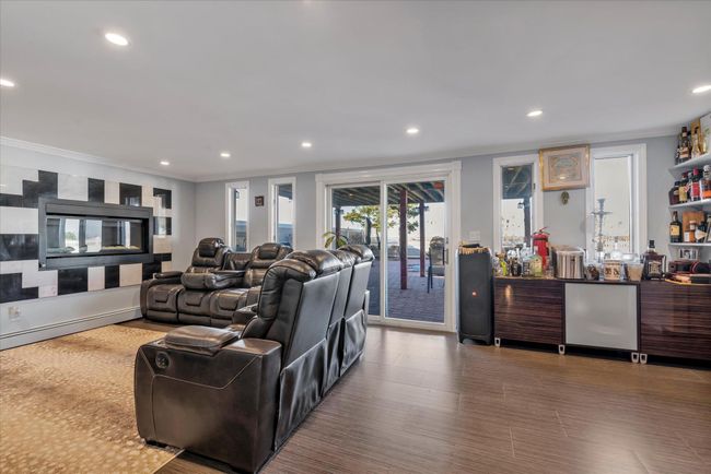 Family room with doors to backyard, featuring wood finished floors, a fireplace, recessed lighting, a bar, and ornamental molding | Image 11