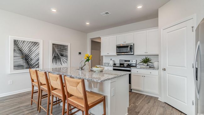 Kitchen featuring appliances with stainless steel finishes, light wood-style floors, a center island with sink, white cabinetry, and light stone countertops | Image 10