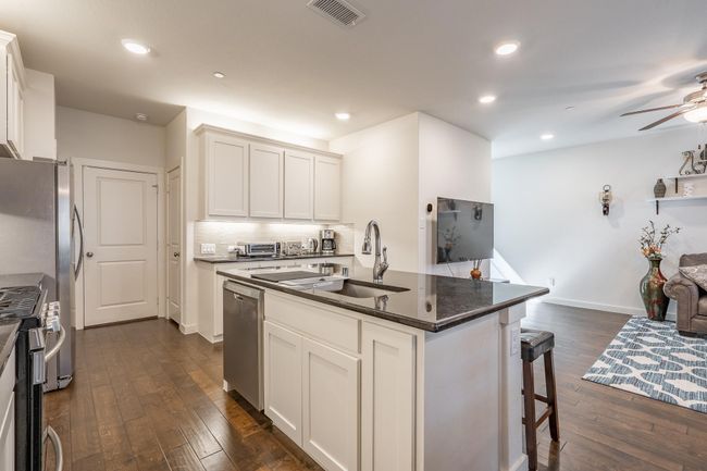 Kitchen featuring visible vents, appliances with stainless steel finishes, a sink, dark countertops, and dark wood-style floors | Image 10