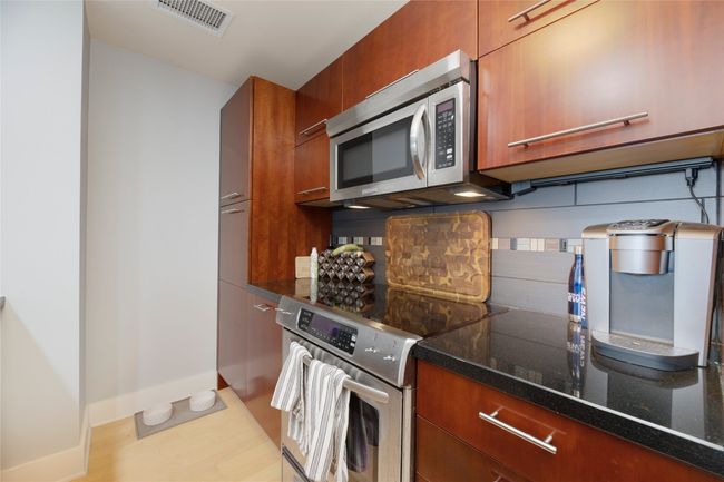 Kitchen with stainless steel appliances, dark stone countertops, brown cabinetry, and light wood finished floors | Image 11