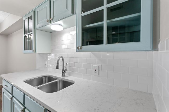 Kitchen featuring light stone counters, a sink, glass insert cabinets, and tasteful backsplash | Image 16