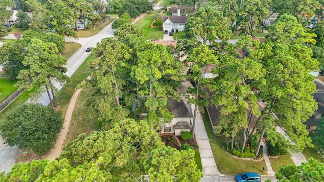 This aerial photo showcases a charming home nestled among tall trees in a lush, green neighborhood. The property features a well-maintained driveway and is situated on a quiet, winding street, offering a serene and private setting. | Image 26