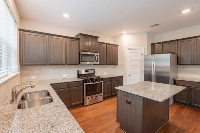 Kitchen with decorative backsplash, visible vents, appliances with stainless steel finishes, a sink, and light wood-style floors | Image 7