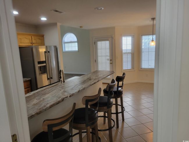 Kitchen with stainless steel refrigerator with ice dispenser, tile patterned floors, a breakfast bar area, light brown cabinets, and recessed lighting | Image 31