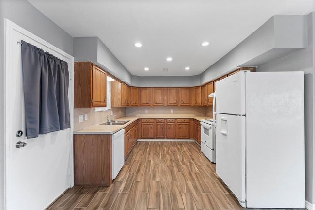 Spacious kitchen with wood cabinets, modern appliances, and wood-look flooring. Ample counter space and recessed lighting enhance functionality. | Image 16