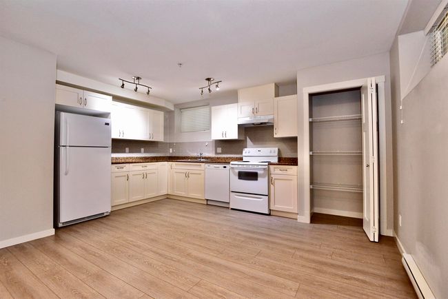 Kitchen with white appliances, under cabinet range hood, baseboard heating, dark countertops, and white cabinetry | Image 32