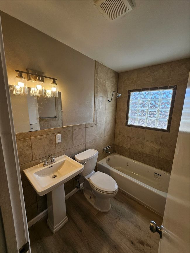 Bathroom with wood finished floors, visible vents, shower / bath combination, tile walls, and toilet | Image 8