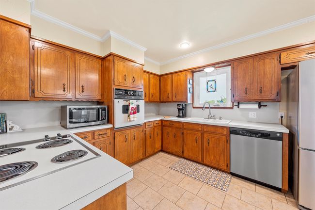Kitchen featuring stainless steel appliances, brown cabinetry, ornamental molding, light countertops, and light tile patterned floors | Image 13