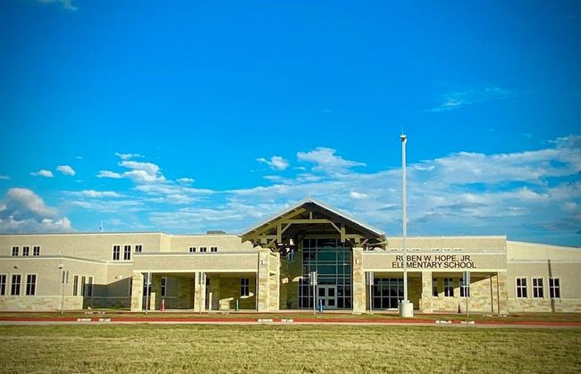 In neighborhood modern elementary school building with a large entrance and a flagpole in front, set against a clear blue sky. The area appears well-maintained, suggesting a family-friendly neighborhood and convenience for early education years | Image 14