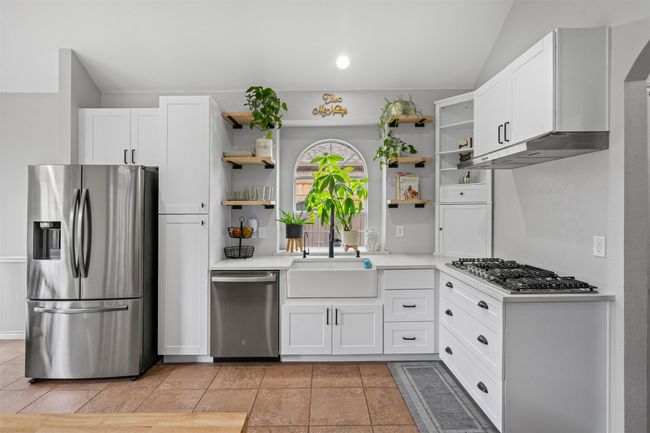Kitchen featuring stainless steel appliances, open shelves, light countertops, vaulted ceiling, and white cabinetry | Image 15