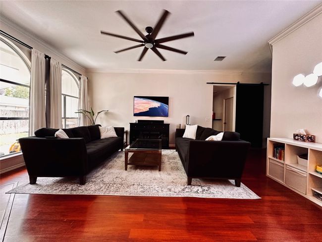 Living area featuring crown molding, ceiling fan, visible vents, a barn door, and wood finished floors | Image 4