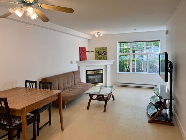 Living area featuring a baseboard heating unit, a ceiling fan, a glass covered fireplace, and light wood-style flooring | Image 9