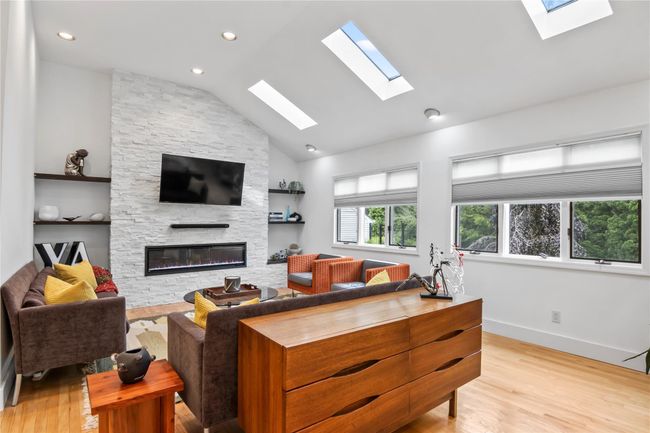 Living area with a skylight, a fireplace, light wood-type flooring, lofted ceiling, and baseboards | Image 12