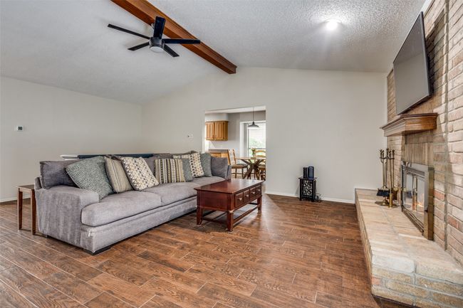 Living room with a ceiling fan, a brick fireplace, wood finished floors, and a textured ceiling | Image 6