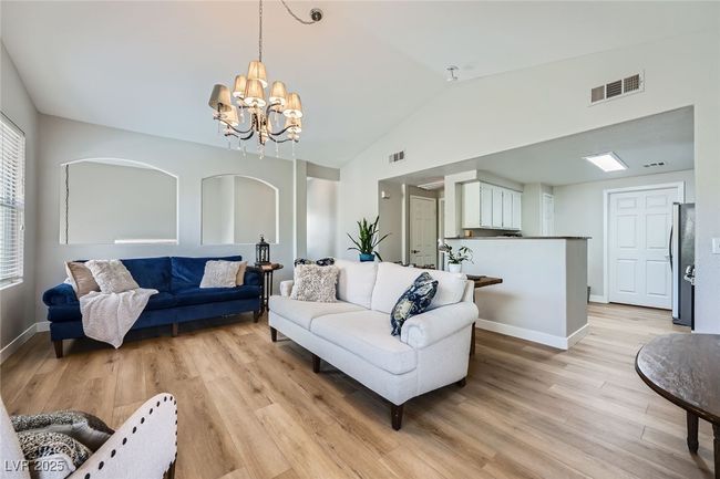 Living area featuring lofted ceiling, an inviting chandelier, visible vents, light wood-type flooring, and baseboards | Image 4