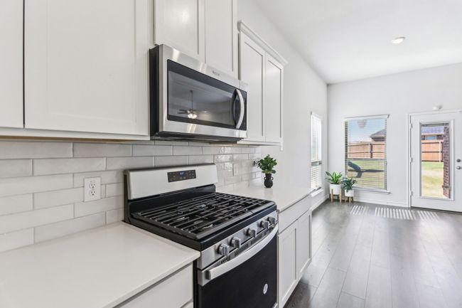 Kitchen featuring white cabinets, appliances with stainless steel finishes, wood finished floors, light countertops, and backsplash | Image 13
