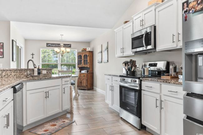 Kitchen featuring stainless steel appliances, a chandelier, white cabinetry, light stone counters, and hanging light fixtures | Image 10