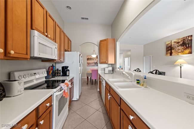 Kitchen featuring arched walkways, a sink, visible vents, white appliances, and light tile patterned floors | Image 9