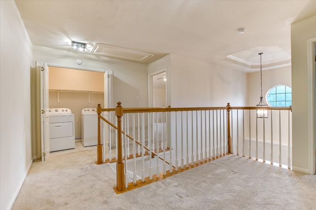 Hallway featuring attic access, independent washer and dryer, carpet flooring, an upstairs landing, and baseboards | Image 10