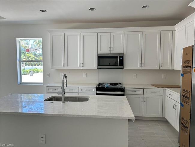 Kitchen featuring white cabinetry, light stone countertops, a kitchen island, stainless steel appliances, and sink | Image 6