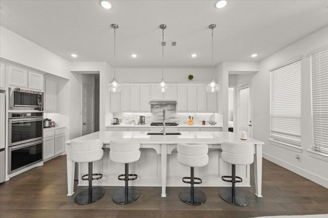 Kitchen featuring double oven, light countertops, decorative backsplash, a kitchen bar, and dark wood-style floors | Image 8