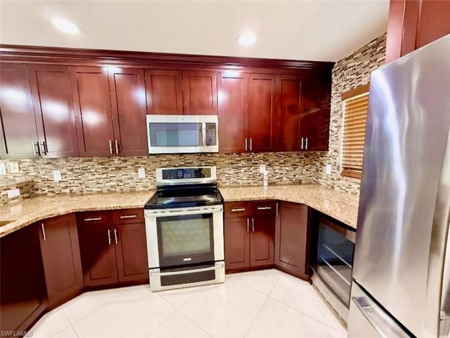 Kitchen with light tile patterned floors, dark brown cabinets, appliances with stainless steel finishes, and tasteful backsplash | Image 13