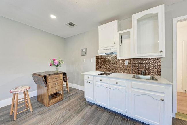Kitchen featuring visible vents, backsplash, under cabinet range hood, white cabinets, and a sink | Image 34