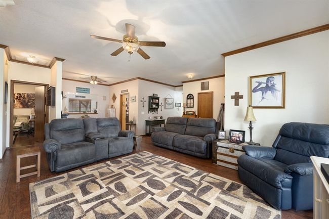 Living area with ceiling fan, wood finished floors, and crown molding | Image 11