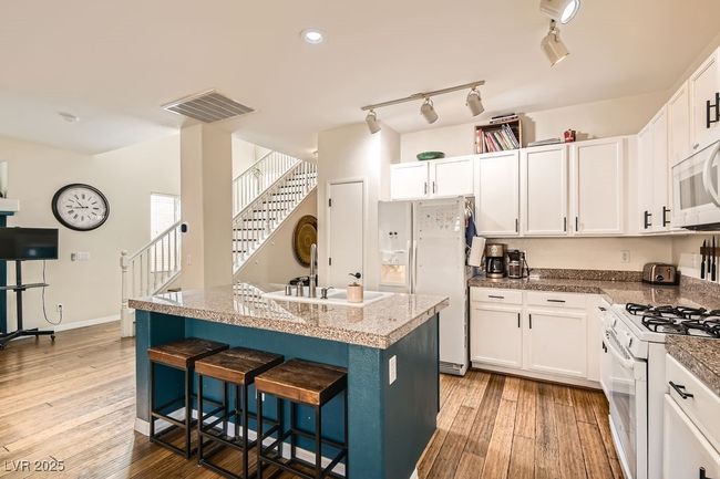 Kitchen featuring a breakfast bar area, white appliances, a sink, visible vents, and wood finished floors | Image 8