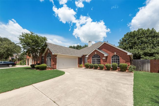 View of front facade with brick siding, a garage, driveway, a chimney, and roof with shingles | Image 5
