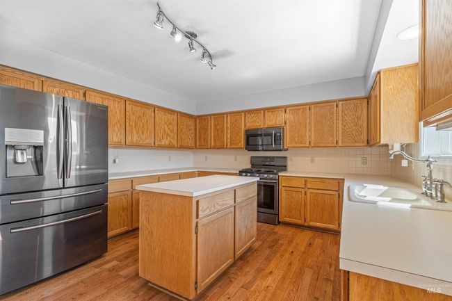 Kitchen featuring appliances with stainless steel finishes, light countertops, a kitchen island, light wood-style flooring, and tasteful backsplash | Image 5