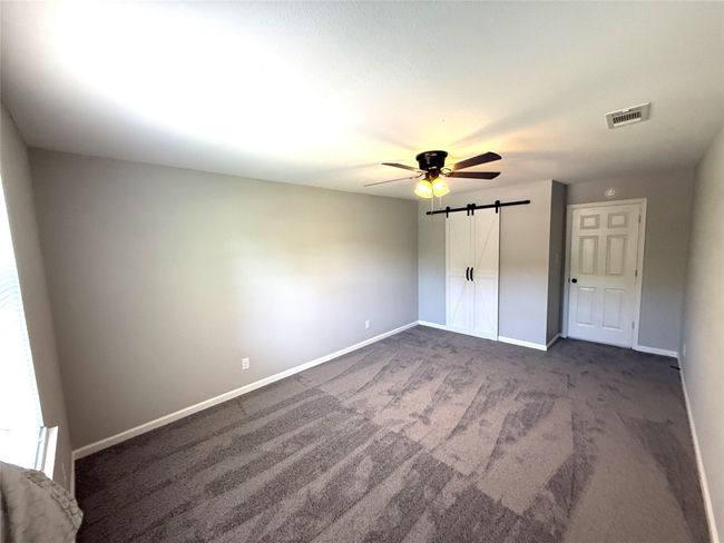 Unfurnished bedroom with a barn door, ceiling fan, baseboards, visible vents, and dark carpet | Image 9