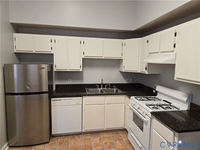 Kitchen featuring white appliances, white cabinetry, under cabinet range hood, and dark stone countertops | Image 8
